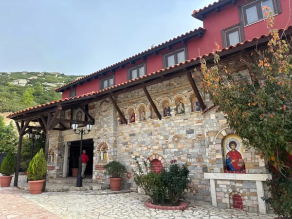 Saint Panteleimon Monastery features a stone façade with arched windows, vibrant icon paintings, and lush greenery at Mount Pentelicus, Attica.