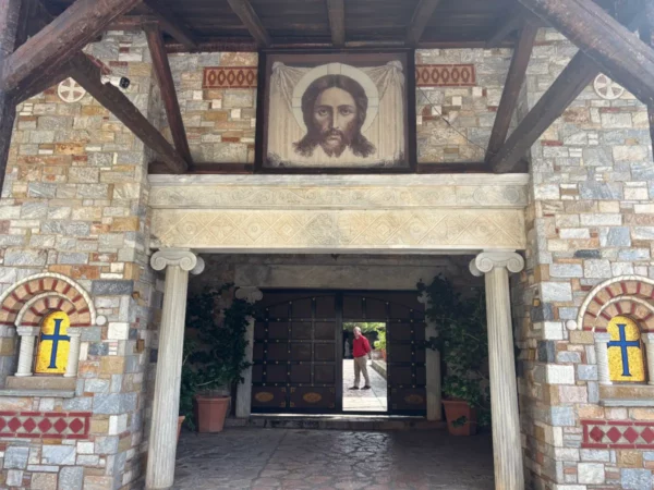 Entrance to Saint Panteleimon Monastery features stone walls and a large icon of Christ, surrounded by greenery in Mount Pentelicus, Attica.