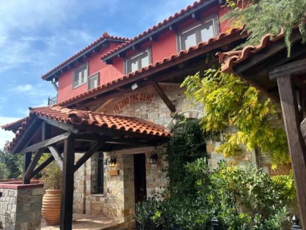 Charming stone building with a red-tiled roof, surrounded by green foliage at Saint Panteleimon Monastery, Mount Pentelicus, Attica, Greece.