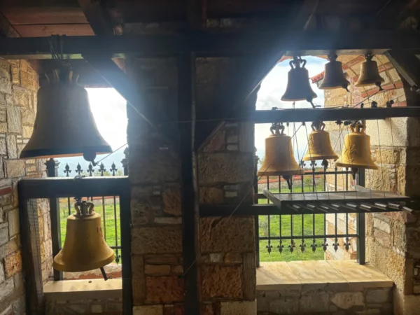 Golden bells hang in the bell tower of Saint Panteleimon Monastery, with views of lush greenery on Mount Pentelicus, Attica, Greece.