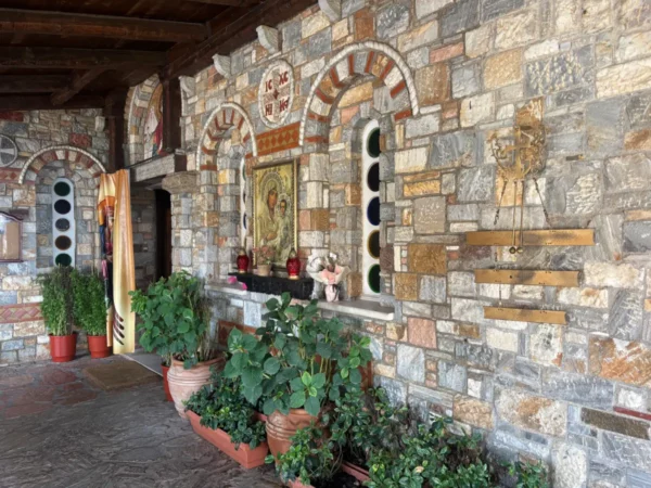 Rustic stone walls adorned with colorful mosaics and religious icons, featuring potted plants at Saint Panteleimon Monastery, Mount Pentelicus.