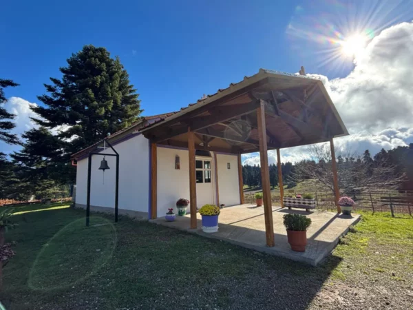 The church of Saints Anargyroi in Tanaida with a covered porch, surrounded by potted plants under bright blue skies