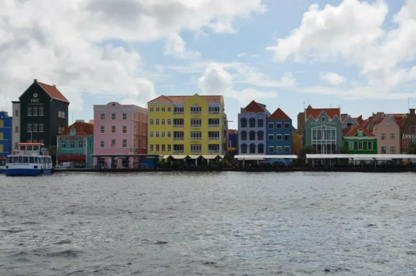 Colorful buildings line the waterfront in The famous Handelskade waterfront, Willemstad, Curacao, showcasing vibrant hues against a cloudy sky.