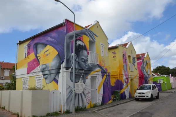 Vibrant street art adorns the walls of colorful buildings inKaya Kaya Street Art Square, Willemstad, showcasing striking murals and a lively neighborhood atmosphere.