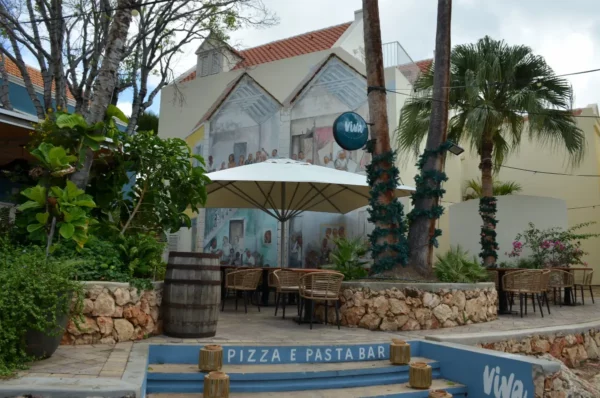 Charming outdoor dining area in Willemstad, Curacao, featuring a mural, palm trees, and cozy seating under an umbrella.