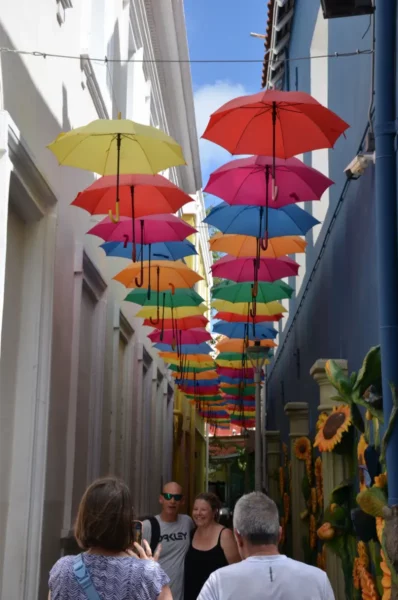 Colorful umbrellas in vibrant hues hang overhead along a narrow street in Willemstad, Curaçao, creating a festive atmosphere.