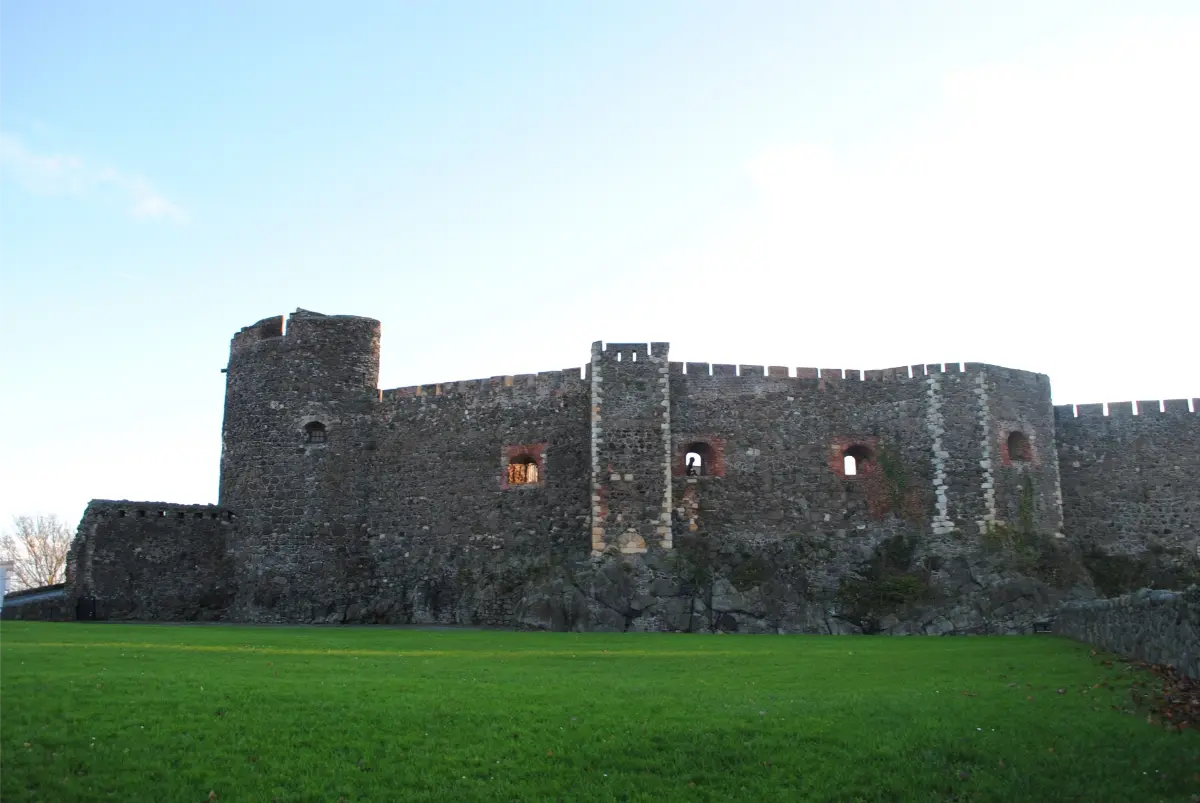 Historic stone castle with towers surrounded by lush green grass in Belfast, Northern Ireland, under a clear blue sky.