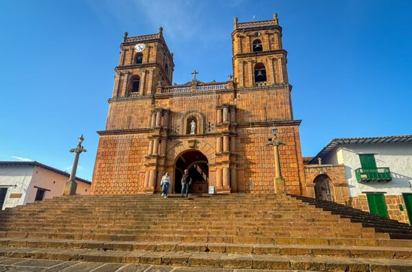 The iconic San Gil Church in Barichara features striking terracotta walls and a grand staircase under a clear blue sky.