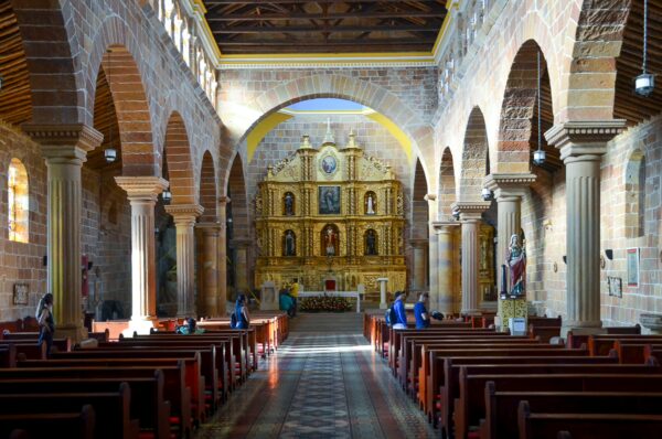 Interior of a historic church in Barichara, featuring detailed archways, wooden pews, and a vibrant altar adorned with gold accents.