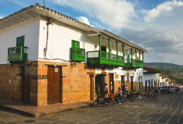 Charming white colonial buildings with green balconies line a cobblestone street in Barichara, Santander, Colombia.