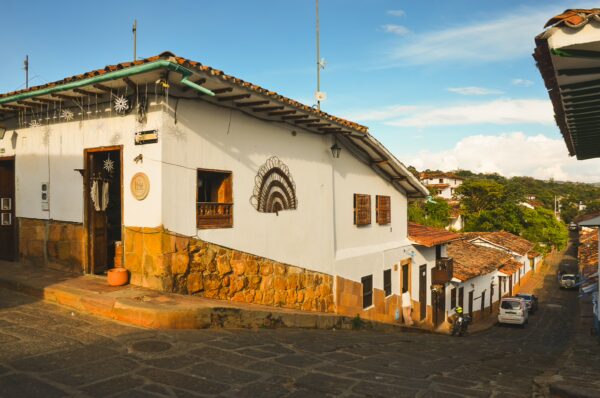 Charming colonial houses with terracotta roofs line the cobblestone streets of Barichara, surrounded by lush green hills.