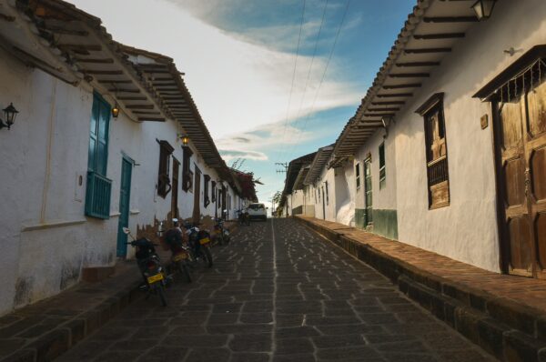 Quaint cobblestone street in Barichara, Santander, lined with whitewashed houses and colorful doors under a clear sky.