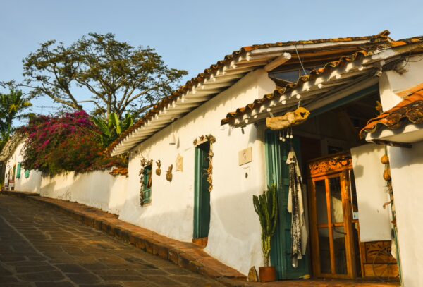 Charming whitewashed houses with blue doors and vibrant bougainvillea line the cobblestone street in Barichara, Colombia.