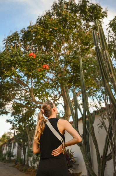 A woman gazes at vibrant flowers on trees lining a pathway in Barichara, Santander, Colombia, framed by tall cacti.
