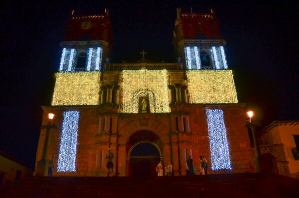 Barichara's Cathedral of the Immaculate Conception lit up at night in the main square, with visitors standing on the steps
