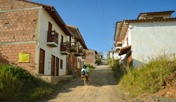 Dirt road in southern Barichara lined with whitewashed houses and brick buildings, with a motorbike heading uphill