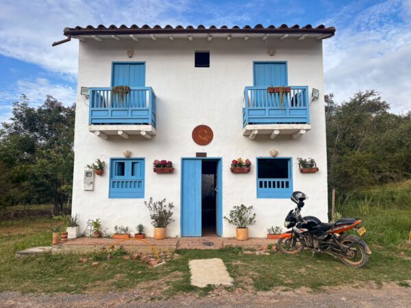 White colonial-style house with bright blue doors and balconies in Barichara, Colombia, set among greenery