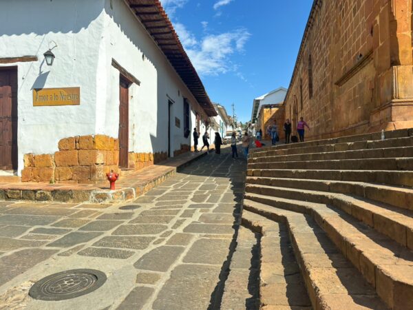 Charming cobblestone streets of Barichara, Colombia, lined with whitewashed buildings and warm golden stone walls under a bright blue sky.