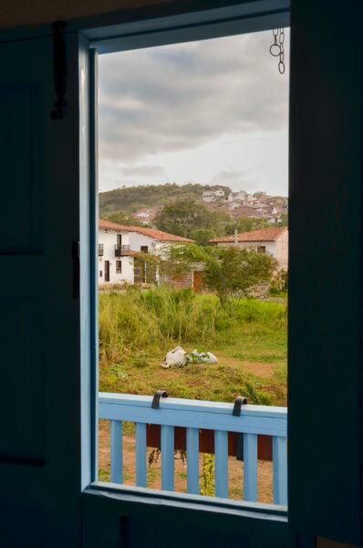 A scenic view from a blue window frame, showcasing green hills and colorful houses in Barichara, Santander, Colombia.