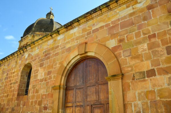 Stunning yellow sandstone wall and wooden door of a historic church in Barichara, Santander, Colombia, under a bright blue sky.