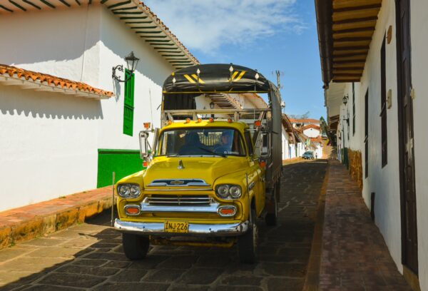 Yellow truck on a narrow cobblestone street lined with white colonial buildings in Barichara, Colombia