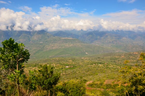 Panoramic view of lush green hills and mountains under a blue sky with scattered clouds, showcasing the beauty of Barichara, Santander.