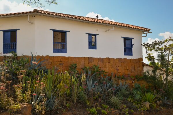 Charming white house with blue windows nestled on a hillside, surrounded by vibrant plants in Barichara, Santander, Colombia.