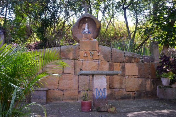 A serene stone altar with a small statue is surrounded by lush greenery in Barichara, Santander, Colombia.
