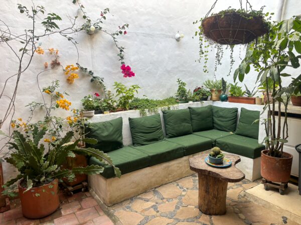 A cozy guesthouse courtyard in Barichara with green cushioned seating, potted plants, and whitewashed walls