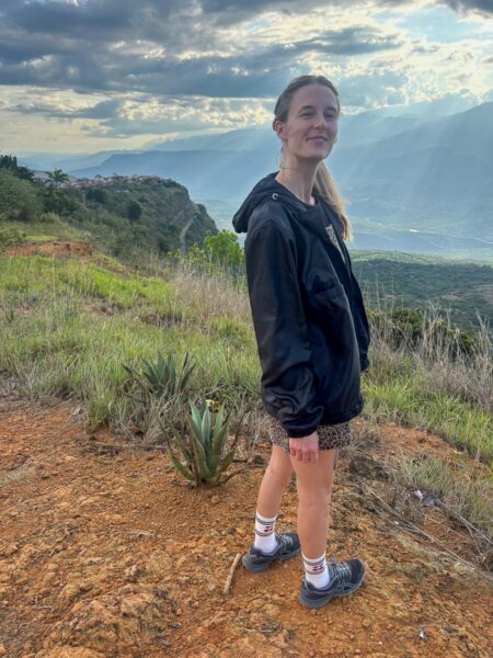 Standing on a hillside near Barichara, a traveler poses with lush green mountains and dramatic clouds in the background.