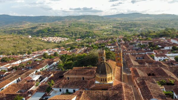 Aerial view of Barichara, Colombia, showcasing terracotta roofs, green hills, and the distinctive yellow dome of a church.