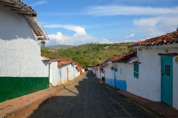 Charming narrow street in Barichara, Santander, lined with whitewashed buildings and colorful doors, under a bright blue sky.
