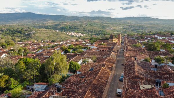 Aerial view of Barichara, Colombia, showcasing charming clay-tiled roofs and lush green hills under a cloudy sky.