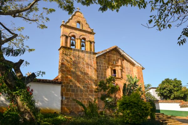 Stone jesus chapel in Barichara with a bell tower, surrounded by trees and a small garden