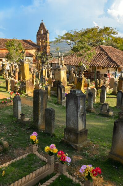 Colorful flowers adorn tombstones in Barichara's cemetery, with a picturesque chapel and rolling hills in the background.