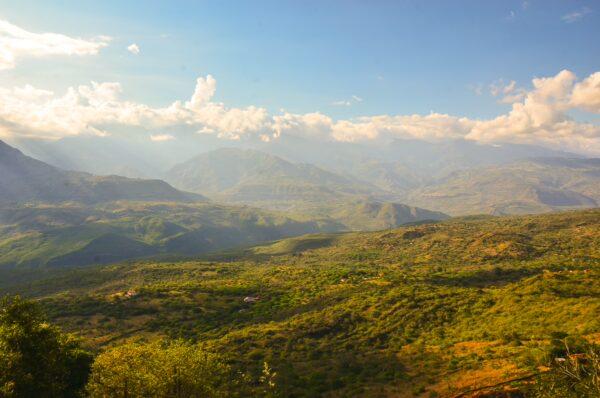 Lush green mountains and valleys under a bright blue sky in the landscape of Barichara, Santander, Colombia.