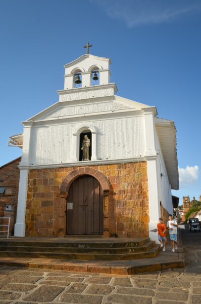 San Antonio Chapel in Barichara, with whitewashed walls, a stone base, arched doorway, and bell tower against a blue sky