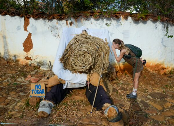 A traveler leans in to inspect a playful siesta sculpture beside a white wall in Barichara, Santander, Colombia