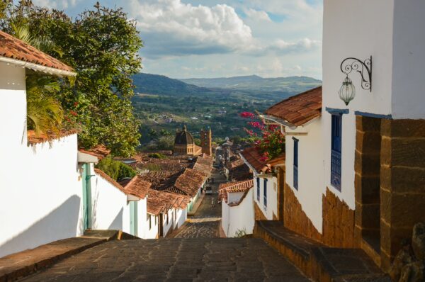 Steep cobblestone street in Barichara with whitewashed colonial houses, red-tile roofs, and valley views beyond