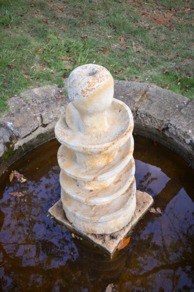 A spiral stone fountain with a shallow pool reflects the greenery around it in Barichara, Santander, Colombia.