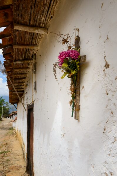 Colorful flowers decorate a wooden cross on a white wall in Guane, Santander, highlighting local craftsmanship and charm.