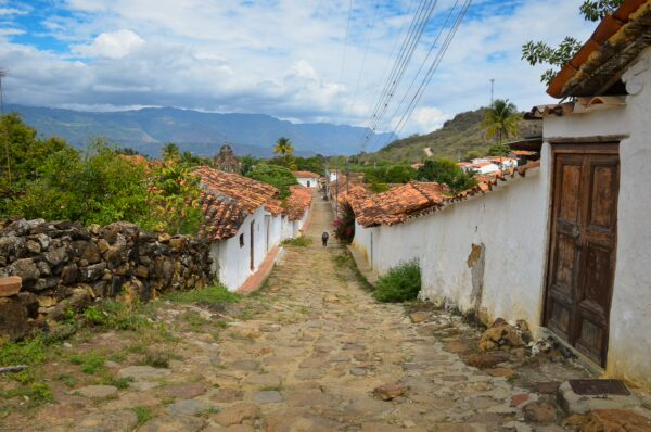 Charming cobblestone street in Guane, Santander, Colombia, lined with whitewashed buildings and vibrant greenery under a blue sky.
