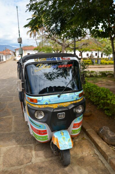 A colorful tuk-tuk parked along a cobblestone street in Guane, Santander, Colombia, surrounded by greenery and traditional buildings.