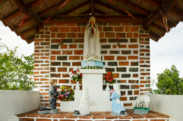 A small shrine featuring a statue of a woman in white, surrounded by colorful flowers and smaller figures in Guane, Santander.