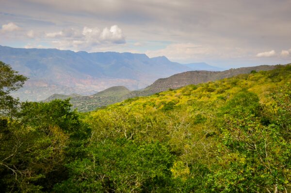 Lush green hills and mountains stretch across the landscape near Guane, Villanueva, Santander, Colombia under a cloudy sky.