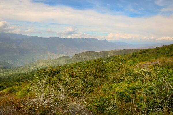 Rolling green hills and mountains under a blue sky stretch across the landscape near Guane, Santander, Colombia.