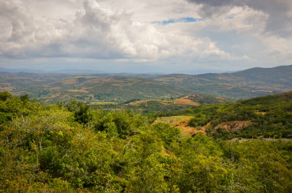 Lush green hills stretch across the landscape near Guane, Santander, under a cloudy sky, showcasing Colombia's natural beauty.