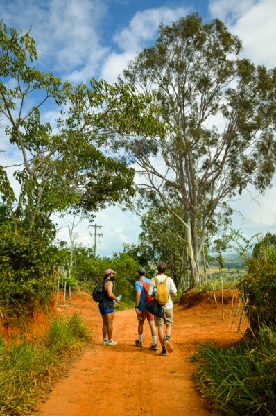 Three hikers explore a sandy path surrounded by lush greenery and tall trees in Guane, Santander, Colombia.