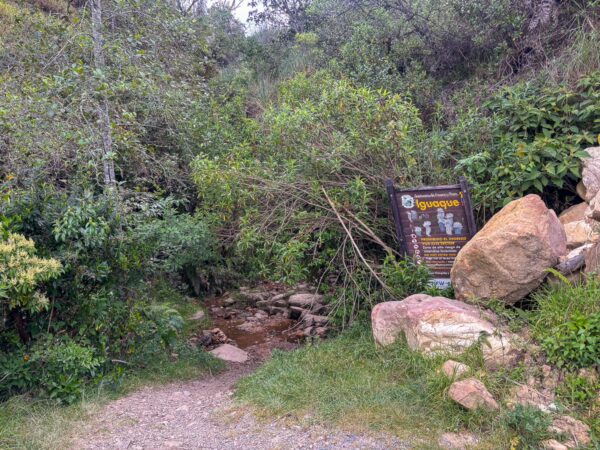 Trailhead sign beside a stream at the entrance to Camino de Herradura in Iguaque National Park, Boyacá, Colombia