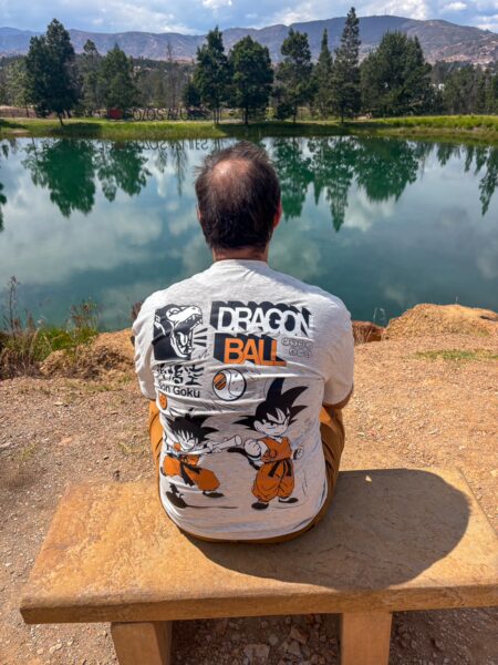 Person wearing a Dragon Ball Z T-shirt sitting on a bench overlooking a turquoise lake at Pozos Azules, Villa de Leyva, Boyacá, Colombia